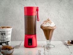 a blender sitting on top of a table next to a cup filled with ice cream