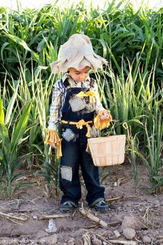 a young boy wearing overalls and holding a basket with flowers on it in front of some plants