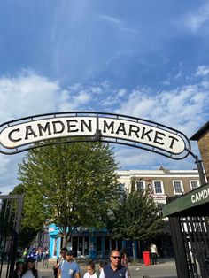 people walking under the camden market sign on a sunny day with blue skies in the background