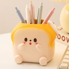 a cute little cat shaped pencil holder with pens in it's mouth, next to a keyboard