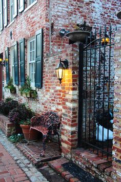 an old brick building with wrought iron fence and bench on the sidewalk next to it