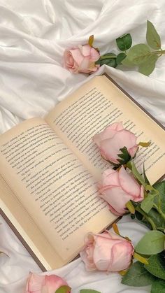 an open book sitting on top of a bed next to pink roses