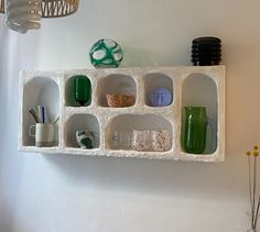 a white shelf with cups and vases on top of it next to a wall