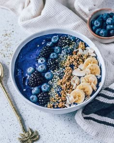 a bowl filled with blueberries, banana slices and granola next to a spoon