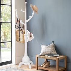 a white coat rack with hats on it next to a bench and rug in front of a blue wall