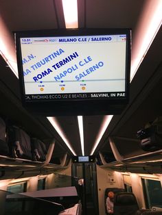 an empty train car with people sitting on the seats in front of it and a large screen above them