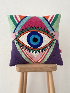 a pillow with an eye on it sitting on a wooden stool in front of a white wall