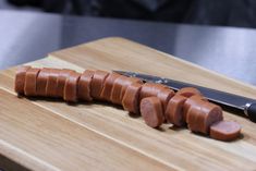 a wooden cutting board topped with sliced up hot dogs next to a knife on top of it