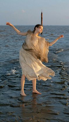 a woman standing in the water with her arms spread out and holding an umbrella over her head