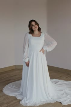 a woman in a white dress standing on a wooden floor with her arms behind her back