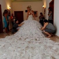 a woman in a wedding dress is being worked on by another woman who is kneeling down