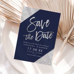 save the date card on a plate next to fan and palm tree leaves in shades of blue with silver glitter