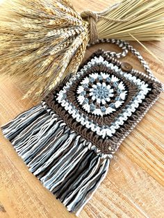 a crocheted square with tassels is sitting on a wooden table next to a broom