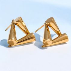 These elegant stainless steel earrings feature a geometric triangle design and are gold-plated for a luxurious finish. Weighing 6 grams each, they measure 14/15 cm in length, making them a striking accessory for any outfit. Weight: 6g. Material: 18K PVD Gold Plated Stainless Steel. Care Instructions:  * Protect your jewelry from scratches.  * Avoid exposure to harsh chemicals.  * Store your jewelry away from direct sunlight in a microfiber pouch.  * Clean with warm water and detergent-free soap; Gold Triangle Minimalist Earrings, Minimalist Gold Triangle Earrings, Gold Triangle Metal Earrings, Triangle Gold Metal Earrings, Modern Triangle Earrings For Party, Modern Triangle Party Earrings, Modern Triangle Metal Earrings, Triangle Stud Earrings, Triangle Earrings Stud