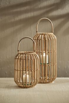 two wicker lanterns with candles in them sitting on a wooden table next to a wall