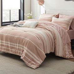 a bed with pink and white striped comforter in a bedroom next to a window