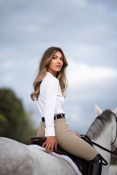 a beautiful young woman riding on the back of a white horse in a dress shirt