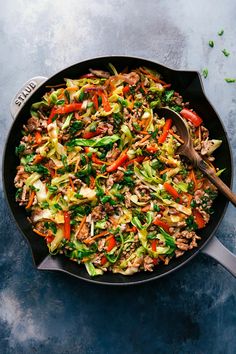 a skillet filled with stir fry vegetables on top of a blue countertop next to a wooden spoon