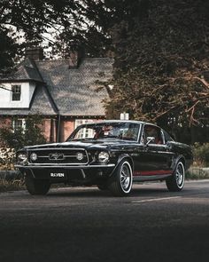 an old mustang is parked on the side of the road in front of a house