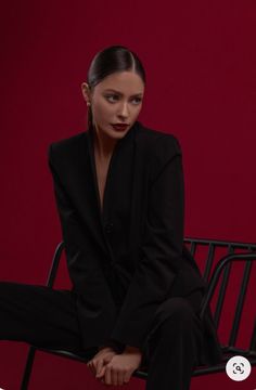 a woman sitting on top of a chair wearing a black suit and matching heels with her hair in a bun