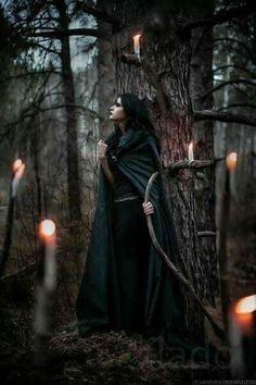 a woman dressed in black standing next to a tree and holding a stick with candles on it