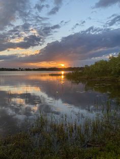 the sun is setting over a lake with tall grass