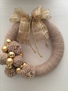 a wreath with gold balls and tassels hanging on the wall next to a ribbon