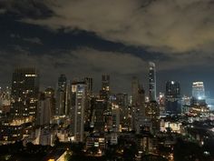 the city skyline is lit up at night with clouds in the sky and lights on