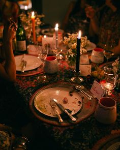 people sitting at a dinner table with plates and silverware on it, lit candles in the background