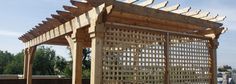 a wooden pergolated structure sitting on top of a cement ground next to trees