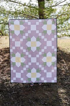 a woman standing in front of a tree with a purple and green quilt on it