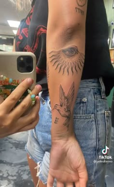 a person with a bird tattoo on their arm holding a cell phone and taking a selfie