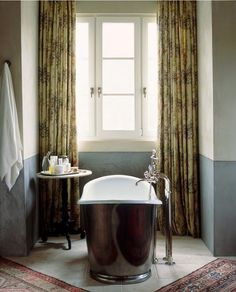 a bath tub sitting under a window next to a table with a cup on it