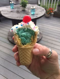 a hand holding an ice cream cone with green and blue frosting, topped with a cherry