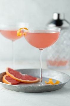 two cocktail glasses with grapefruit and blood orange garnish sit on a silver plate