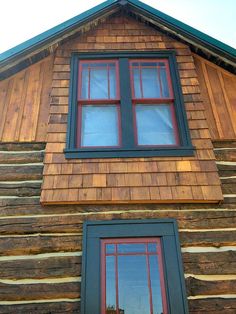 a wooden building with two windows and a cat sitting on the window sill