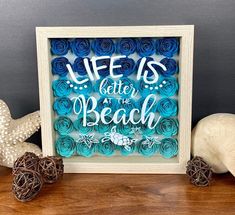 a wooden frame with blue paper flowers and sea shells on the table next to it