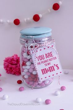 a jar filled with pink and white candies next to a string of pom - poms