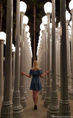 a woman in a blue dress is walking through an array of white columns and lamps