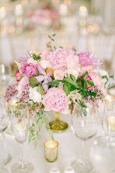 a vase filled with pink and white flowers on top of a table next to wine glasses