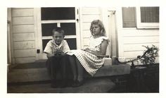 an old black and white photo of two children sitting on the front step of a house