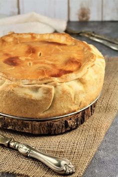 a pie sitting on top of a wooden table next to a knife and spoons