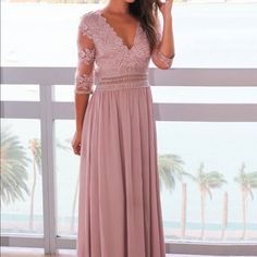 a woman in a long pink dress standing on a balcony with palm trees and water behind her