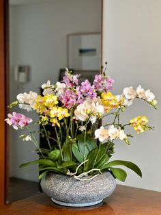 a vase filled with flowers sitting on top of a wooden table next to a mirror