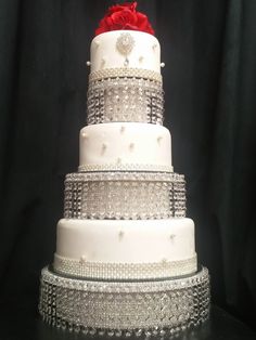 a white wedding cake with red rose on top and silver beading around the edges