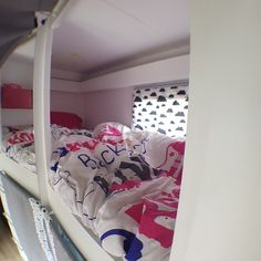 a bunk bed with white sheets and pink pillows in a small room filled with other items