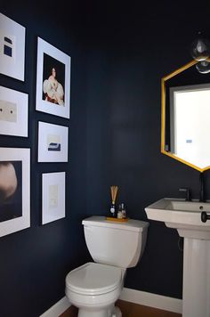 a white toilet sitting next to a sink in a bathroom under pictures on the wall