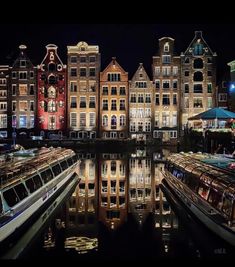 several boats are parked in front of some buildings at night, with lights reflecting on the water