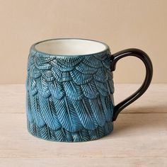 a coffee mug with blue leaves on it sitting on a table next to a wall