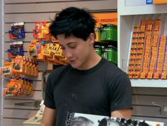 a young man holding a book in front of a shelf with orange juices on it